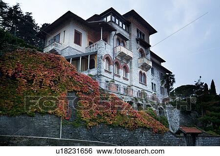 Stock Photograph - Front and side view of large, multilevel old house in Northern italy with stone facade, ornate arched windows, painted balconies and painted exterior, Northern italy. Fotosearch