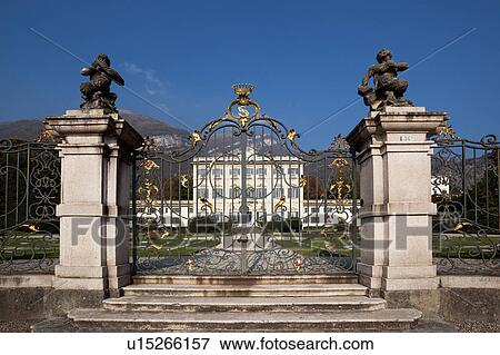 Stock Photo - Front of Renaissance villa, white stucco with ornate decoration around grey shuttered windows and balconies, ornamental gardens with flower beds, steps leading to ornate gold and black wrought iron gates with bronze statues on matching columns, Lake Como. Fotosearch