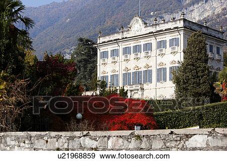 Front of Renaissance villa, white stucco with ornate decoration around grey shuttered windows and balconies, ornamental gardens with foliage bright red, green hedges an cypress trees, Lake Como, Northern Italy View Large Photo Image Stock Photo - Front of Renaissance villa, white stucco with ornate decoration around grey shuttered windows and balconies, ornamental gardens with foliage bright red, green hedges an cypress trees, Lake Como, Northern Italy. Fotosearch
