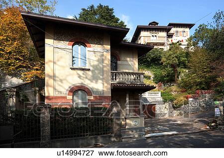 Front view of large, multilevel old house with coach house, in Northern italy with stone facade, ornate arched windows, painted balconies and painted exterior, trees surrounding with autumn foliage on sunny afternoon, Northern Italy View Large Photo Image Stock Photo - Front view of large, multilevel old house with coach house, in Northern italy with stone facade, ornate arched windows, painted balconies and painted exterior, trees surrounding with autumn foliage on sunny afternoon, Northern Italy. Fotosearch