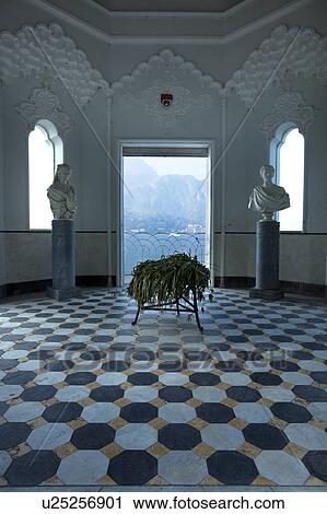 Stock Image - Interior of Tempio at Villa Melzi with ornate stucco interior, black and white geometric pattern of floor, arched windows and doorway with view onto Lake Como, sunlit autumn afternoon, Northern Italy. Fotosearch