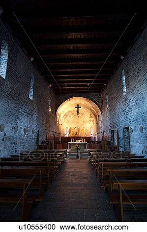 Stock Image - Interior view of nave of Abbey, Piona, Lake Como, Northern Italy, showing stone walls and flat wooden beam ceiling, with altar illuminated, and frescoed apse. Fotosearch