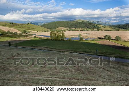 Stock Image - Italian farmland with rolling hills, road, river, on sunny spring afternoon. Fotosearch