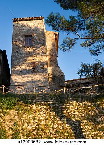 Stock Image - Medieval convent tower rising above village stone ramparts in late afternoon summer sunlight, Umbria. Fotosearch