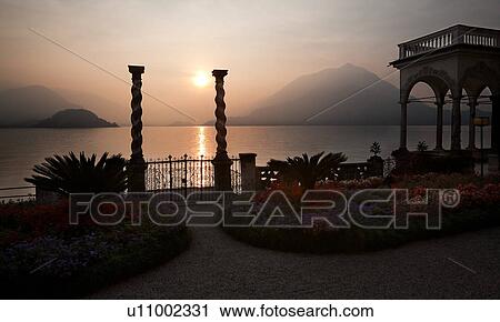 Ornamental gardens of Villa Monastero with carved stone wall, flower beds, and terracotta pots on columns, with view overlooking Lake Como and mountain range beyond, autumn afternoon with blue sky View Large Photo Image Stock Image - Ornamental gardens of Villa Monastero with carved stone wall, flower beds, and terracotta pots on columns, with view overlooking Lake Como and mountain range beyond, autumn afternoon with blue sky. Fotosearch
