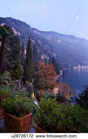 Ornamental gardens of Villa Monastero with terracotta pots on columns, with view overlooking town of Varenna, Lake Como and mountain range beyond, autumn evening at dusk with moonrise and blue sky, Northern Italy View Large Photo Image Stock Image - Ornamental gardens of Villa Monastero with terracotta pots on columns, with view overlooking town of Varenna, Lake Como and mountain range beyond, autumn evening at dusk with moonrise and blue sky, Northern Italy. Fotosearch