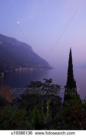 Ornamental gardens of Villa Monastero with view overlooking town of Varenna, Lake Como and mountain range beyond, autumn evening at dusk with moonrise and blue sky, Northern Italy View Large Photo Image Stock Photograph - Ornamental gardens of Villa Monastero with view overlooking town of Varenna, Lake Como and mountain range beyond, autumn evening at dusk with moonrise and blue sky, Northern Italy. Fotosearch