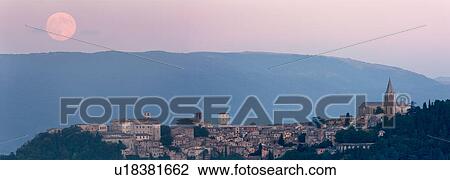 Stock Image - Panorama view of full moon rising over medieval hilltop town of Todi, with spire of San Fortunato, Umbria, Italy. Fotosearch