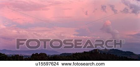 Picture - Panorama view of medieval hilltop town of Todi at sunset, ruined castle tower on tree covered ridge in foreground, distant mountains beyond, with spectacular pink clouds, skyscape, Umbria, Italy. Fotosearch