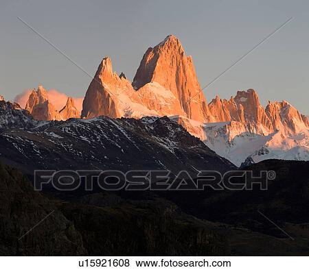 Panorama view of sunrise over the snow covered Andes mountain range, El Chalten, Argentina, Patagonia, with clear blue sky, and mountains of Mount Fitzroy and Cerro Torre reflecting red light of rising sun View Large Photo Image Stock Photo - Panorama view of sunrise over the snow covered Andes mountain range, El Chalten, Argentina, Patagonia, with clear blue sky, and mountains of Mount Fitzroy and Cerro Torre reflecting red light of rising sun. Fotosearch