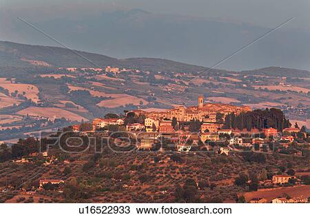 Stock Image - Panoramic view of medieval hilltop town of Monte Castello di Vibio at sunset, with golden light over village and surrounding hills and fields, Umbria, Italy. Fotosearch