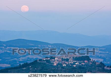 Panoramic view of medieval hilltop town of Monte Castello di Vibio at sunset, hills and fields beyond, with full moon rising over village, pink light, and blue dusk sky, Umbria, Italy View Large Photo Image Stock Photo - Panoramic view of medieval hilltop town of Monte Castello di Vibio at sunset, hills and fields beyond, with full moon rising over village, pink light, and blue dusk sky, Umbria, Italy. Fotosearch