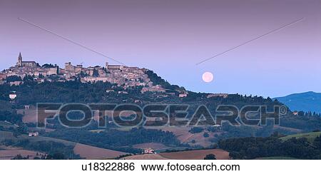 Stock Photograph - Panoramic view of moonset over Todi, Umbria, with medieval hilltop town, full moon in pink sky; farmland in foreground. Fotosearch