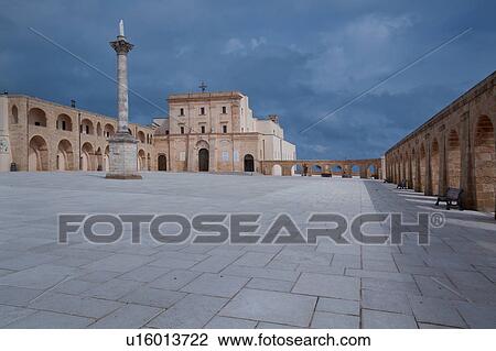Stock Image - Piazza surrounded by arched loggia, with Basilica and Corinthian column on sunny afternoon with stormy sky, Santa Maria di Leuca, Salento, Puglia, Southern Italy. Fotosearch