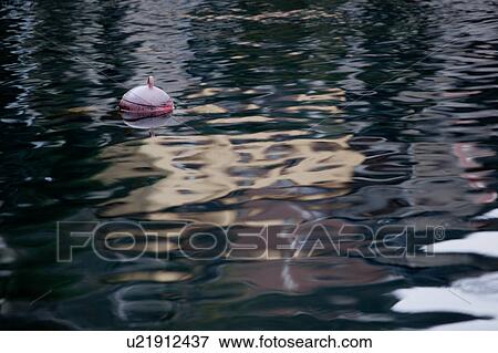 Stock Photo - Pink plastic buoy floating in water, with golden morning light reflected in gentle waves, Lake Como, Northern Italy. Fotosearch