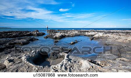 Stock Photo - Rocky beach with bright blue water, fisherman casting in rocky inlet pools, and snow capped mountains of Albania visible across sea, dramatic clouds in blue sky, Salento, Puglia, Southern Italy. Fotosearch