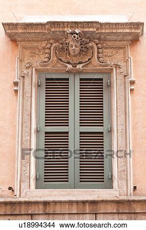 Picture - Rome street, window detail of house, with pink stucco walls, pale green shutters, sculptured head and garlands decorating. Fotosearch