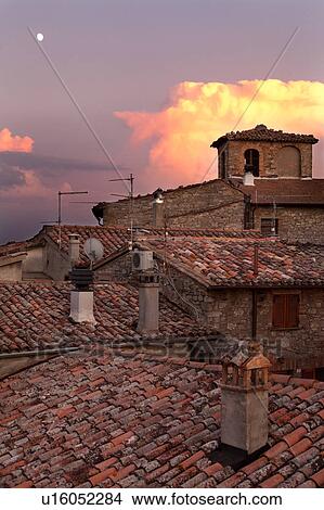 Picture - Rooftop view of Italian village street with houses and roof tiles in foreground, and spectacular sunset with moon rise, Umbria, Italy. Fotosearch