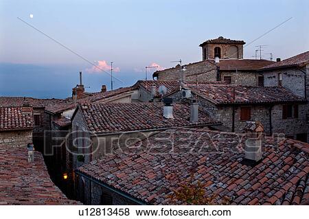 Stock Photo - Rooftop view of Italian village street with houses and roof tiles in foreground, and full moon rising beyond, Umbria, Italy. Fotosearch