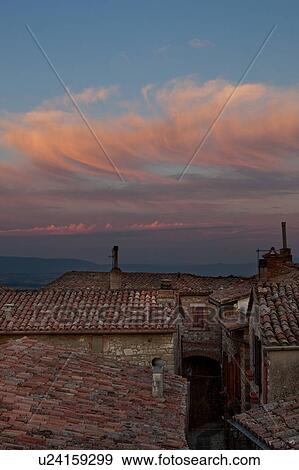 Stock Photo - Rooftop view of Italian village street with houses and roof tiles in foreground and spectacular sunset, and hills beyond, Umbria, Italy. Fotosearch