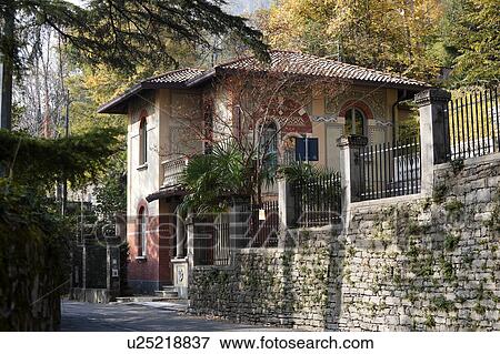 Side view of coach house of villa in Northern italy with stone facade, ornate arched windows, painted balconies and painted exterior, trees surrounding with autumn foliage on sunny afternoon, Northern Italy View Large Photo Image Stock Photo - Side view of coach house of villa in Northern italy with stone facade, ornate arched windows, painted balconies and painted exterior, trees surrounding with autumn foliage on sunny afternoon, Northern Italy. Fotosearch