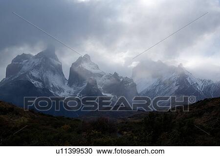 Stock Image - Snow covered Los Cuernos mountains with dramatic autumn cloudscape, fall colours of trees in foreground, Torres del Paine, Southern Chile, Patagonia. Fotosearch