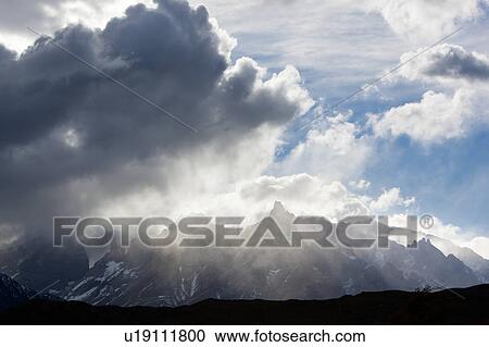 Snow covered Los Cuernos mountains with godbeams and dramatic autumn cloudscape, hills silhouetted in foreground, Torres del Paine, Southern Chile, Patagonia View Large Photo Image Stock Image - Snow covered Los Cuernos mountains with godbeams and dramatic autumn cloudscape, hills silhouetted in foreground, Torres del Paine, Southern Chile, Patagonia. Fotosearch