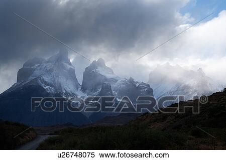 Stock Photography - Snow covered Los Cuernos mountains with dramatic autumn cloudscape, fall colours of trees in foreground, Torres del Paine, Southern Chile, Patagonia. Fotosearch