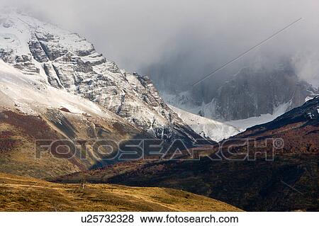 Stock Photo - Snow covered mountains of Las Torres in early morning light, fall colours of scrub grasses and hills in foreground, Torres del Paine, Southern Chile, Patagonia. Fotosearch