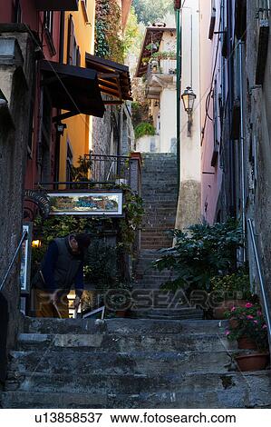 Steep uneven stone stairway up narrow alley with walls of houses painted red/orange in typical evocative style of Northern Italy, man sweeping with broom View Large Photo Image Stock Photo - Steep uneven stone stairway up narrow alley with walls of houses painted red/orange in typical evocative style of Northern Italy, man sweeping with broom. Fotosearch