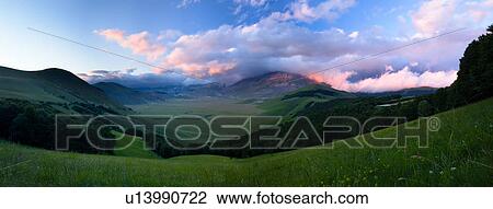Stitched panorama of Piano Grande, Umbria, looking down to green meadow expanse, framed by mountains, pine trees, and billowing pink clouds rolling in at sunset, early summer View Large Photo Image Stock Image - Stitched panorama of Piano Grande, Umbria, looking down to green meadow expanse, framed by mountains, pine trees, and billowing pink clouds rolling in at sunset, early summer. Fotosearch