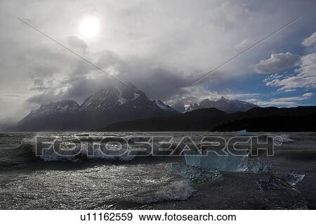 Stock Photo - Stormy grey Lago Grey with blue iceberg fragments blown to shore in heavy winds, dramatic sky, and snow covered mountains in background, Torres del Paine, Southern Chile, Patagonia. Fotosearch