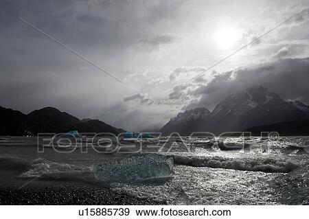 Stormy grey Lago Grey with blue iceberg fragments blown to shore in heavy winds, dramatic sky, and snow covered mountains in background, Torres del Paine, Southern Chile, Patagonia View Large Photo Image Stock Photo - Stormy grey Lago Grey with blue iceberg fragments blown to shore in heavy winds, dramatic sky, and snow covered mountains in background, Torres del Paine, Southern Chile, Patagonia. Fotosearch