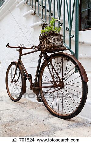 Street detail in Ostuni, with typical white stucco walls, stone paving, metal bicycle chained to wrought iron railing of stairway, with wicker basket of flowers on back, spring afternoon, Salento, Puglia, Southern Italy View Large Photo Image Picture - Street detail in Ostuni, with typical white stucco walls, stone paving, metal bicycle chained to wrought iron railing of stairway, with wicker basket of flowers on back, spring afternoon, Salento, Puglia, Southern Italy. Fotosearch