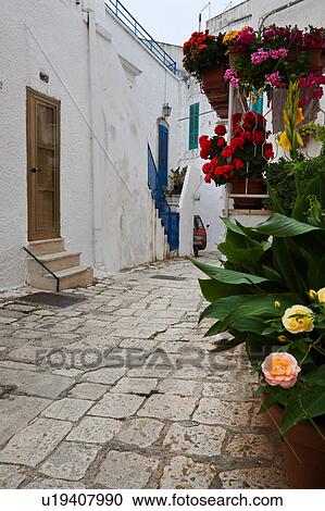 Street in Ostuni, with typical white stucco walls, stone paving, wrought iron lamp, and archway, with flowers decorating, spring afternoon, Salento, Puglia, Southern Italy View Large Photo Image Stock Image - Street in Ostuni, with typical white stucco walls, stone paving, wrought iron lamp, and archway, with flowers decorating, spring afternoon, Salento, Puglia, Southern Italy. Fotosearch