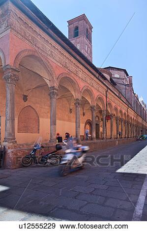 Stock Photo - Street view of ornately decorated portico along side of church of San Giacomo, with people sitting, and motorbike with motion blur, sunny summer morning, Bologna, Italy. Fotosearch