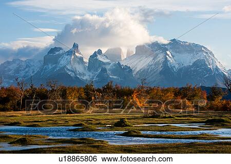 Stock Photograph - Sunrise view of snow covered Los Cuernos, and Towers, Torres del Paine, with dramatic clouds, beech trees in full autumn colours, River Serrano in foreground, Southern Chile, Patagonia. Fotosearch