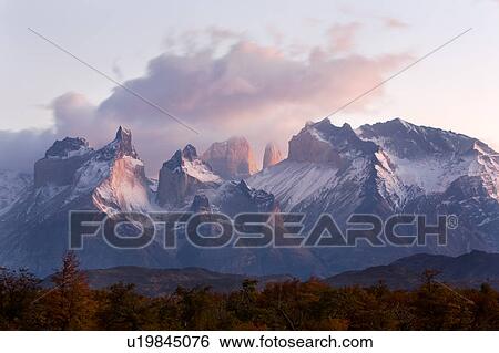 Stock Photograph - Sunrise view of snow covered Los Cuernos, and Towers, Torres del Paine, with dramatic clouds, beech trees in full autumn colours, River Serrano in foreground, Southern Chile, Patagonia. Fotosearch