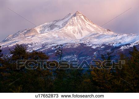 Stock Image - Sunrise view of snow covered mountain range, Torres del Paine, with pink and grey clouds, beech trees in full autumn colours, Southern Chile, Patagonia. Fotosearch
