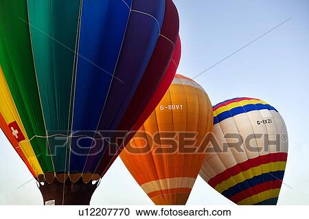 Stock Image - Three overlapping balloons in flight, blue-green, orange, and white with multicloloured stripes, against blue sky. Fotosearch