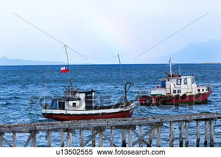 Two fishing boats moored near old wooden pier in choppy blue waters, rainbow and mountains beyond, Puerto Natales, Southern Chile, Patagonia View Large Photo Image Stock Photography - Two fishing boats moored near old wooden pier in choppy blue waters, rainbow and mountains beyond, Puerto Natales, Southern Chile, Patagonia. Fotosearch