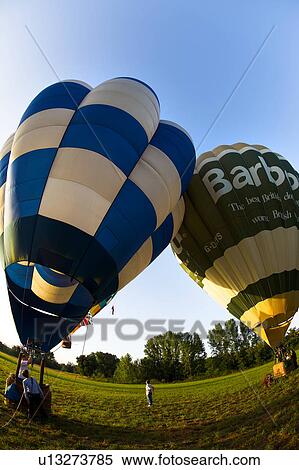 Two hot air balloons rising fom ground with people in baskets and one person standing on grass between the two baskets, sunny morning with blue sky View Large Photo Image Stock Photography - Two hot air balloons rising fom ground with people in baskets and one person standing on grass between the two baskets, sunny morning with blue sky. Fotosearch