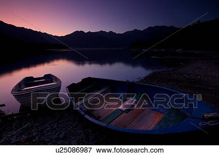 Two traditional wooden fishing boats beached at shore of lake in pink and purple pre-dawn glow, with mountain range and opposite shoreline reflected in calm waters of Lake Como, Northern Italy View Large Photo Image Stock Photo - Two traditional wooden fishing boats beached at shore of lake in pink and purple pre-dawn glow, with mountain range and opposite shoreline reflected in calm waters of Lake Como, Northern Italy. Fotosearch
