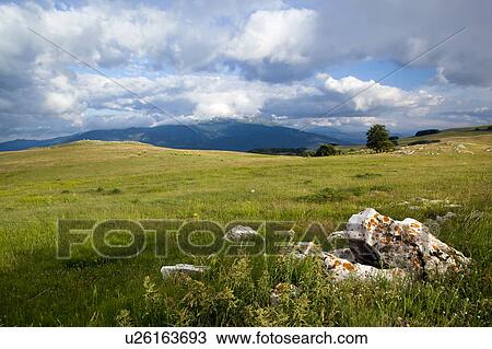 Umbria landscape above Piano Grande, showing meadow on mountain ridge, and view of blue mountains beyond in evening with blue sky, dramatic cloud formation. View Large Photo Image Stock Image - Umbria landscape above Piano Grande, showing meadow on mountain ridge, and view of blue mountains beyond in evening with blue sky, dramatic cloud formation.. Fotosearch