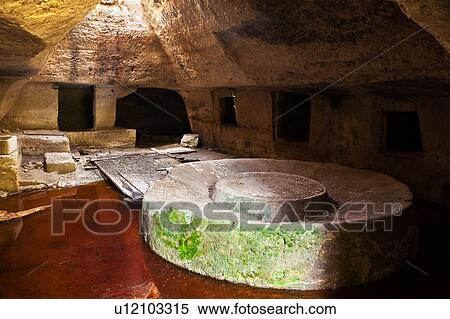 Stock Photography - Underground cavern lit from above, with massive stone grinding wheel and storage, monastery ruin, Salento, Puglia, Southern Italy. Fotosearch