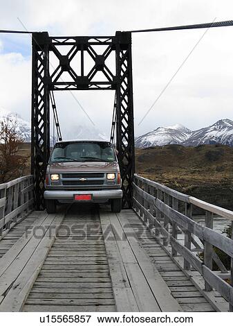 Stock Photo - Van traversing very narrow wooden bridge with metal superstructure, with snow covered mountain range in background, Torres del Paine, Southern Chile, Patagonia. Fotosearch