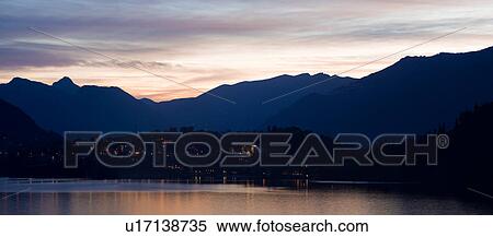 Stock Photography - View across Lake Como at dusk, with beautiful calm sunset colours of blue, purple and pastel pink, mountains silhouetted beyond Bellagio, with town lights illuminated, Lake Como, Northern Italy. Fotosearch