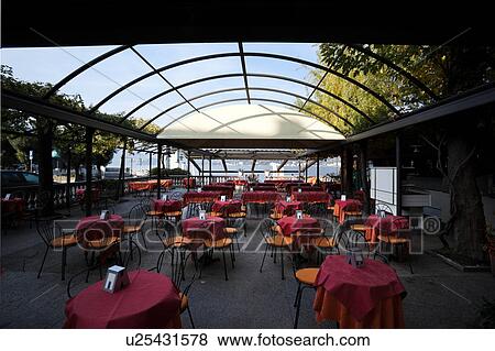 Stock Photo - View of Bellagio lakefront seen from interior of outdoor cafe in early morning sunshine, autumn colours of beech trees, passenger ferry dock, mountain range visible across Lake Como, Northern Italy. Fotosearch