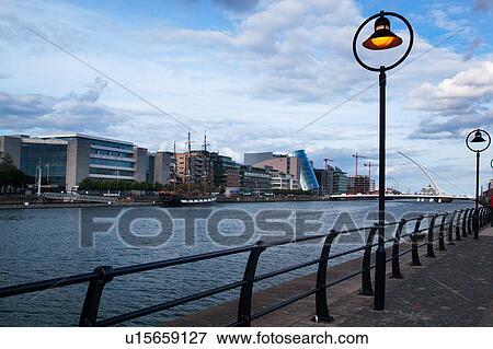 View of Campshire Walk, with wrought iron railings and lit street lamps at sunset with River Liffey, modern buildings of financial district, blue sky and clouds. Dublin, Southern Ireland View Large Photo Image Stock Photo - View of Campshire Walk, with wrought iron railings and lit street lamps at sunset with River Liffey, modern buildings of financial district, blue sky and clouds. Dublin, Southern Ireland. Fotosearch