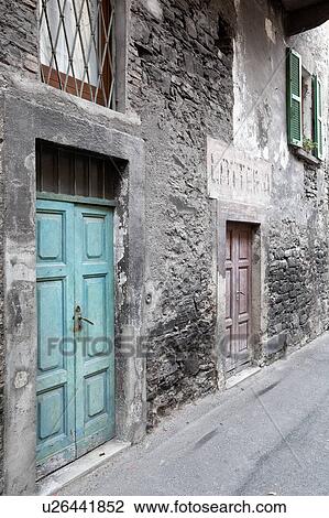 Stock Image - View of Italian village street with delapidated house wih fading paintwork on stone and stucco, old green wooden door, Northern Italy. Fotosearch
